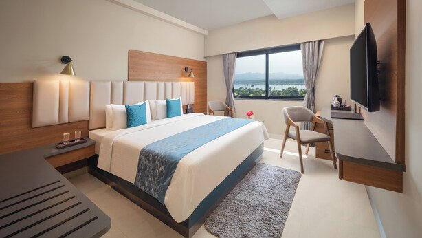 Quarto de hotel moderno com uma cama grande, uma escrivaninha, uma televisão e vista para o exterior.