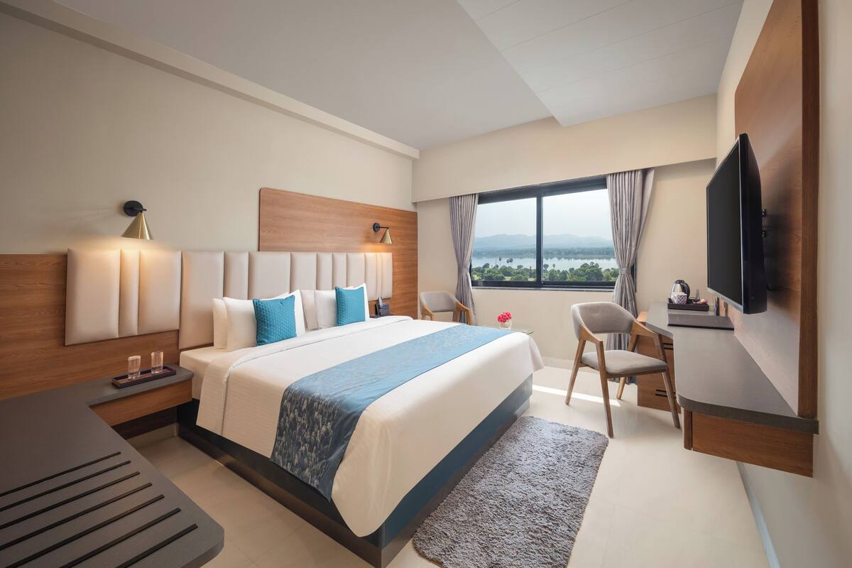 A modern hotel room with a large bed, a desk, a TV, and a view of the outdoors.