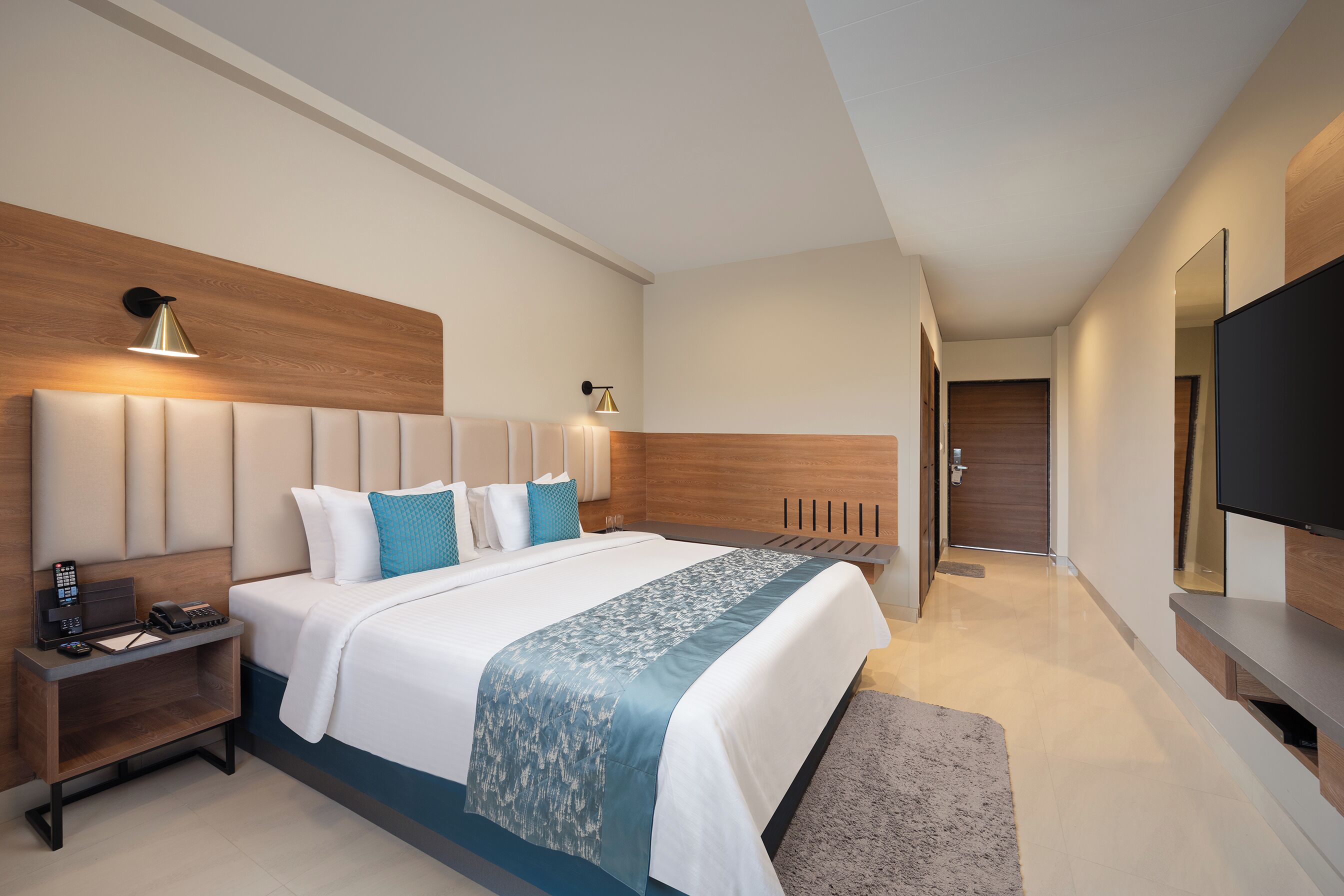 A modern hotel room with a large bed, bedside tables, a flat-screen TV, and a wooden headboard.