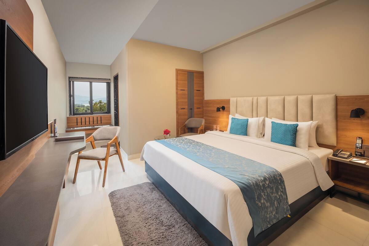 A modern hotel room with a large bed, a desk, a chair, a TV, and a view of the outdoors.