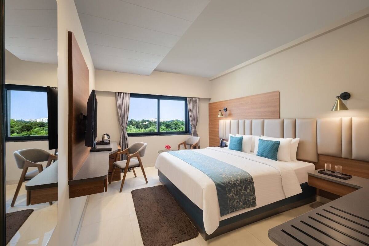 A modern hotel room with a large bed, a desk, a chair, and a TV.