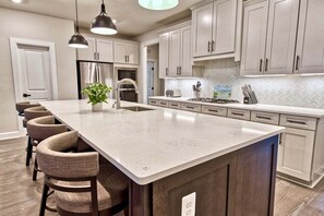 A modern kitchen with a large island, stainless steel appliances, and light-colored cabinetry.