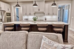 A modern kitchen with a central island, bar stools, pendant lighting, and a view of the adjacent living area.