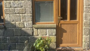 Edificio de piedra con puerta y ventana de madera, plantas en macetas y suelo de grava.