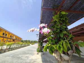 A building with a yellow facade, a covered walkway with potted plants, and a clear sky. - PUENG LUANG RESORT.  (Bang Phae)