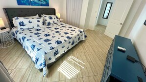Un dormitorio con cama, mesita de noche, cómoda, un cuadro y una puerta.