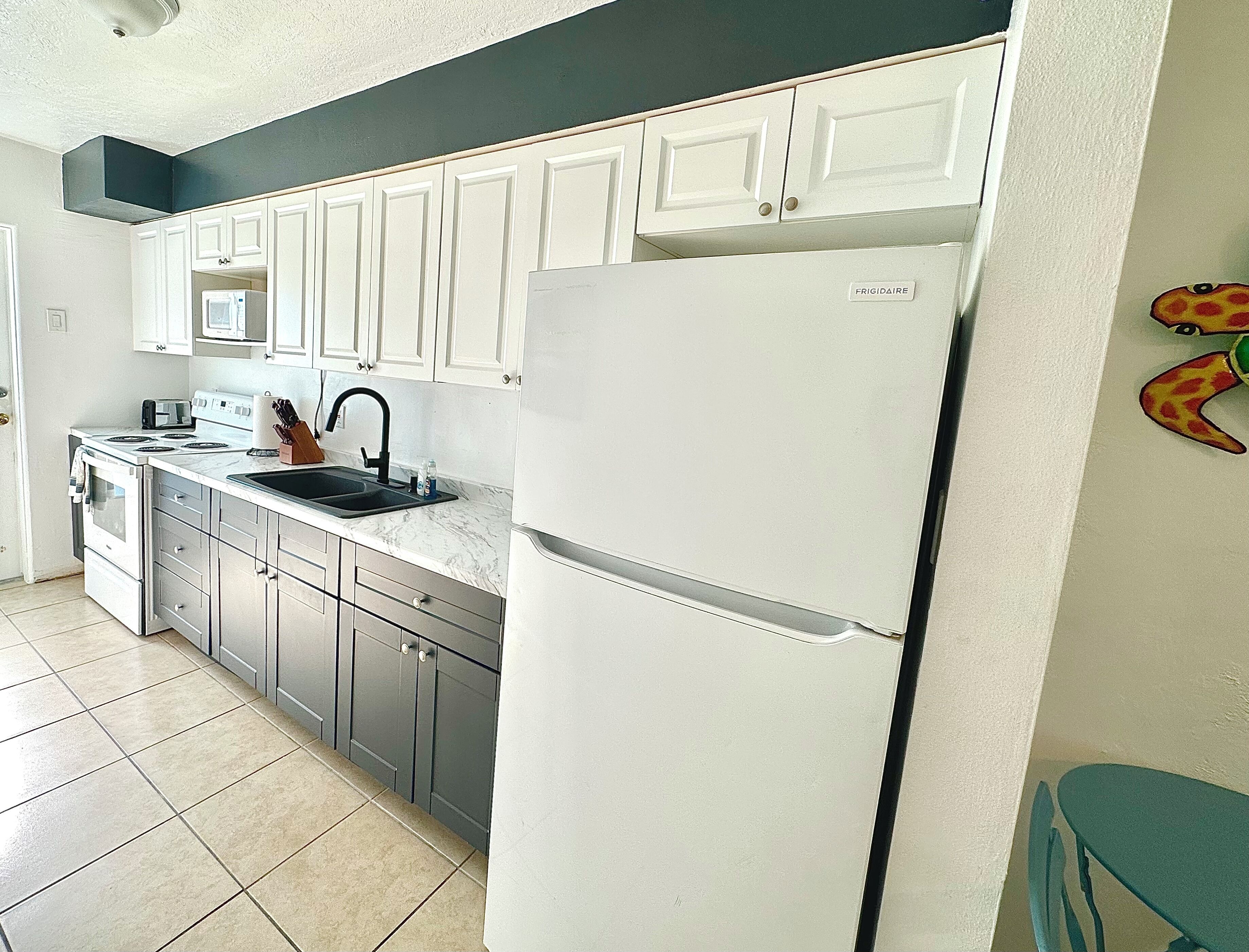 A kitchen with white cabinets, a stainless steel refrigerator, a microwave, and a sink.