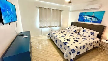 A bedroom with a bed, a desk, a TV, a ceiling fan, and artwork on the walls.