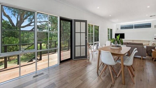 A spacious living area with a large sliding glass door leading to a deck, a dining table with chairs, and a sofa. - Relaxed Sorrento Coastal Living (Sorrento)