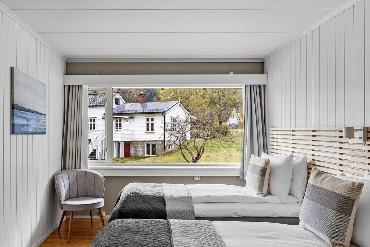 A bedroom with a large window, a bed, a chair, and a painting on the wall.