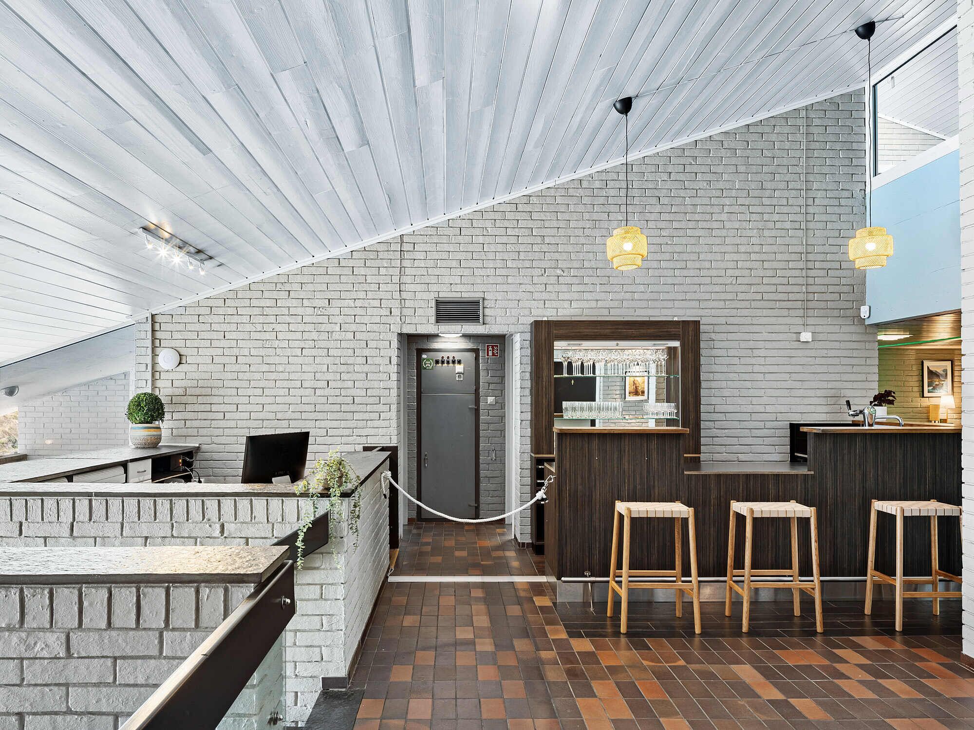 Zona bar moderna con parete in mattoni, sgabelli di legno e un bancone.