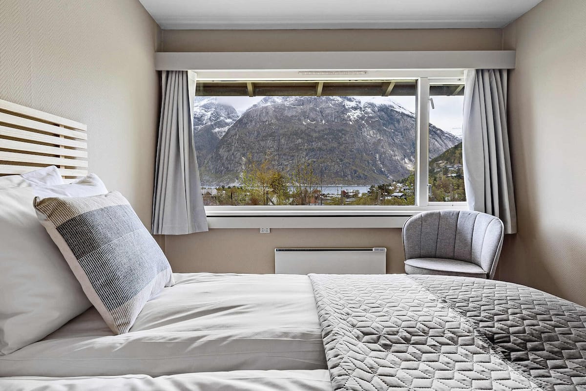 A bedroom with a bed, a chair, and a window with a mountain view.