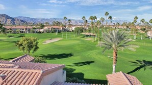 Un campo de golf con vistas a montañas, palmeras y edificios residenciales con techos de tejas rojas.