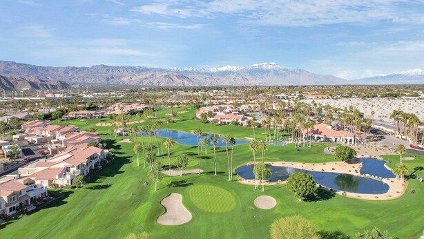 Un campo de golf con varios peligros de agua, rodeado de edificios residenciales y palmeras.