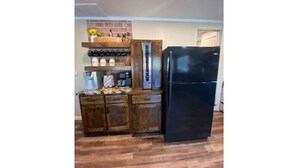 A kitchen with wooden cabinets, a black refrigerator, and a coffee machine. - Cozy riverside cabin on the Neosho river (Chetopa)