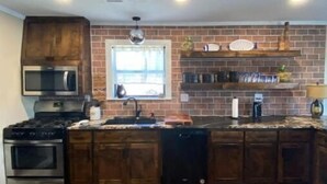 A kitchen with wooden cabinets, a brick backsplash, a stainless steel range, and a window above the sink. - Cozy riverside cabin on the Neosho river (Chetopa)