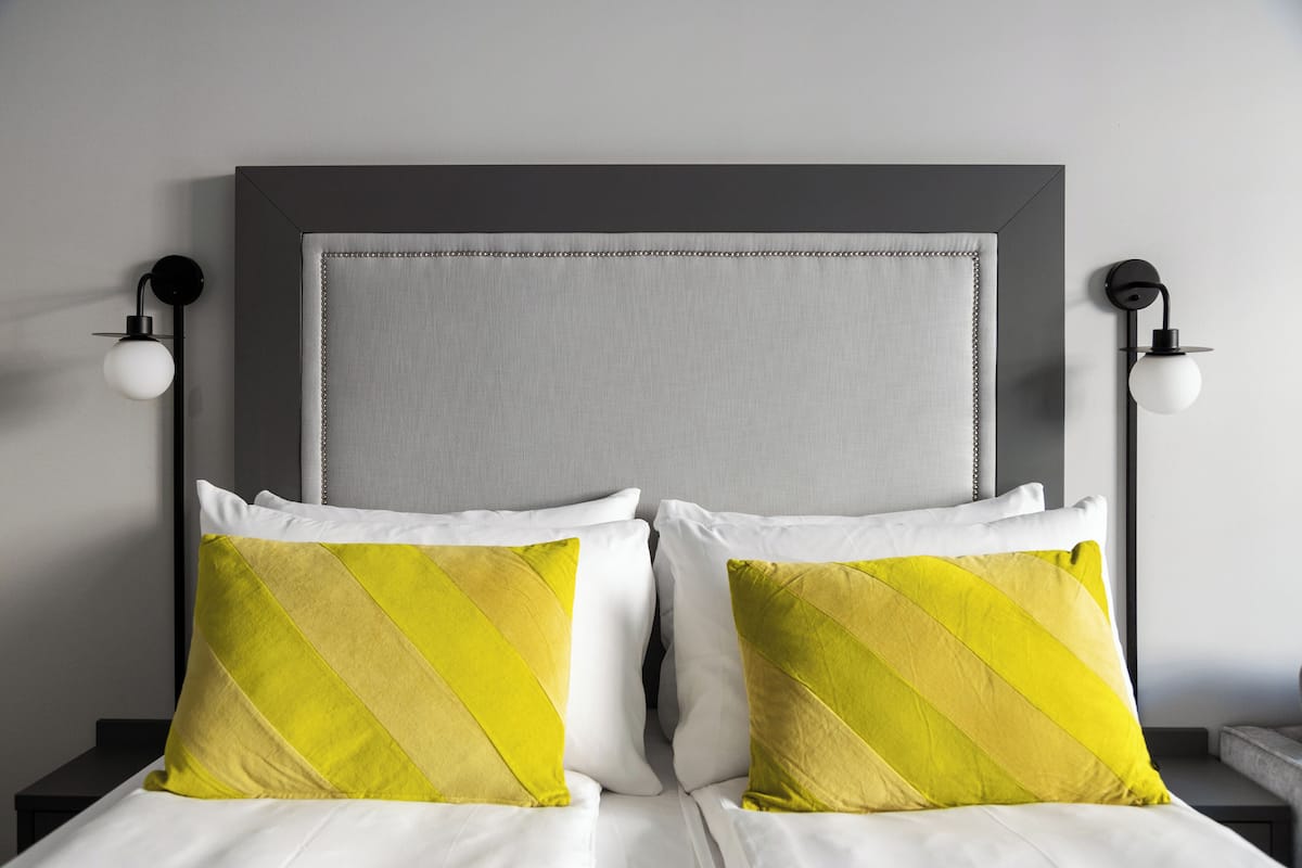 A bed with two pillows, a headboard, and two wall-mounted lamps.
