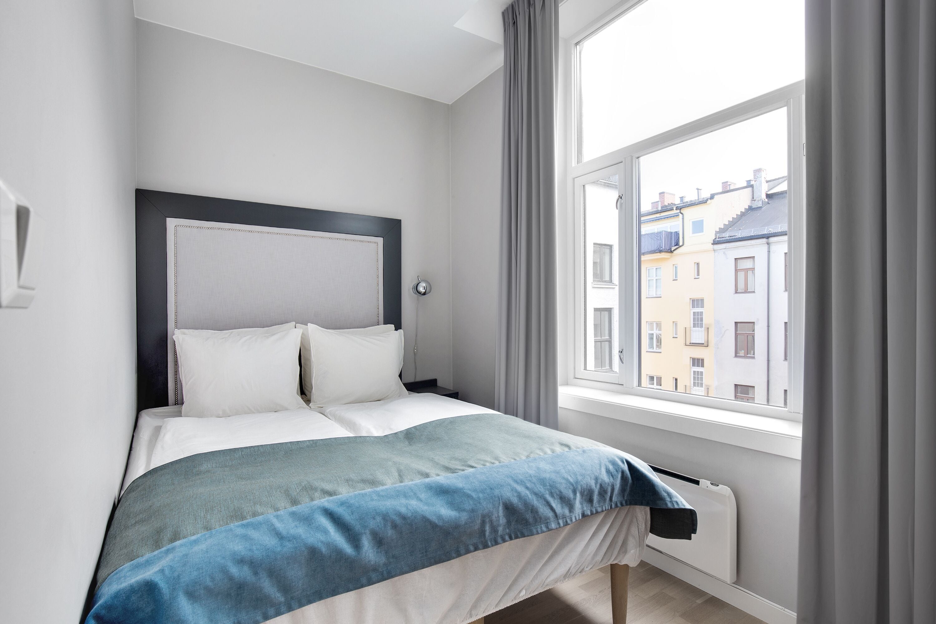 A modern bedroom with a bed, a window with curtains, and a radiator.