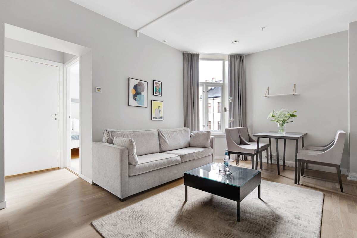 A modern living room with a grey sofa, a glass coffee table, and a dining area with a small table and chairs.