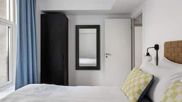A modern bedroom with a bed, a wardrobe, a mirror, and a window with curtains.
