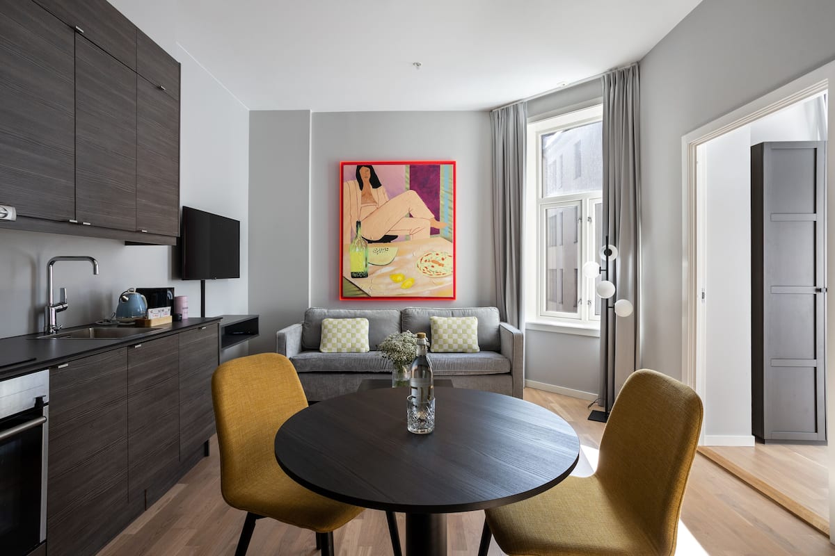 A modern kitchen with dark cabinetry, a dining table with two chairs, and a sofa with cushions.