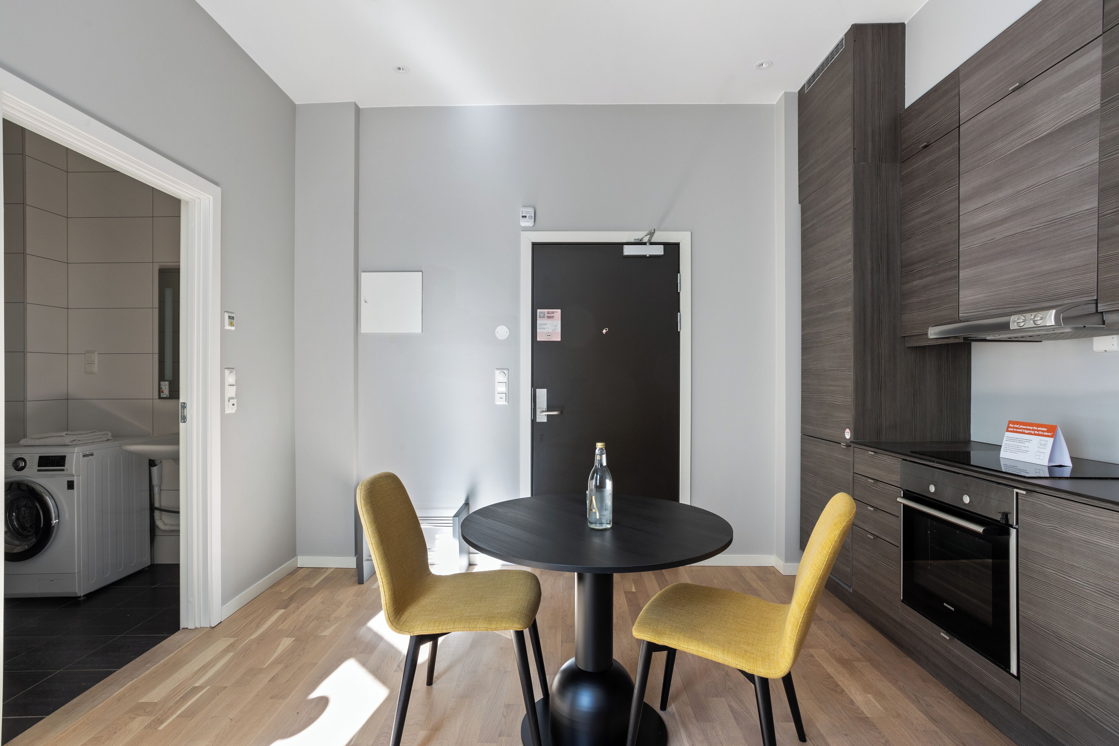 A modern kitchen with dark wood cabinets, a built-in oven, and a round black table with two yellow chairs.