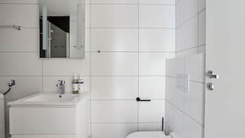 A modern bathroom with white tiles, a sink, a toilet, and a mirror.