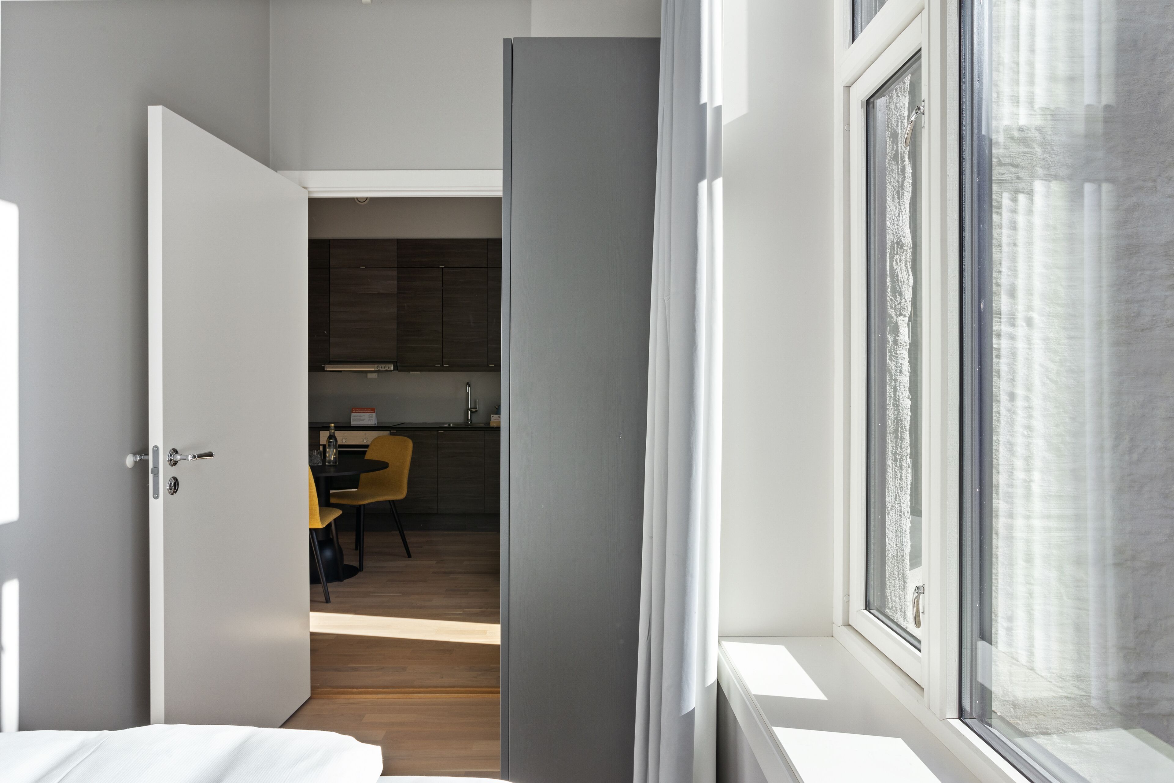 Ein modernes Hotelzimmer mit einem gro ßen Fenster, Holzboden und Blick auf den Küchenbereich.