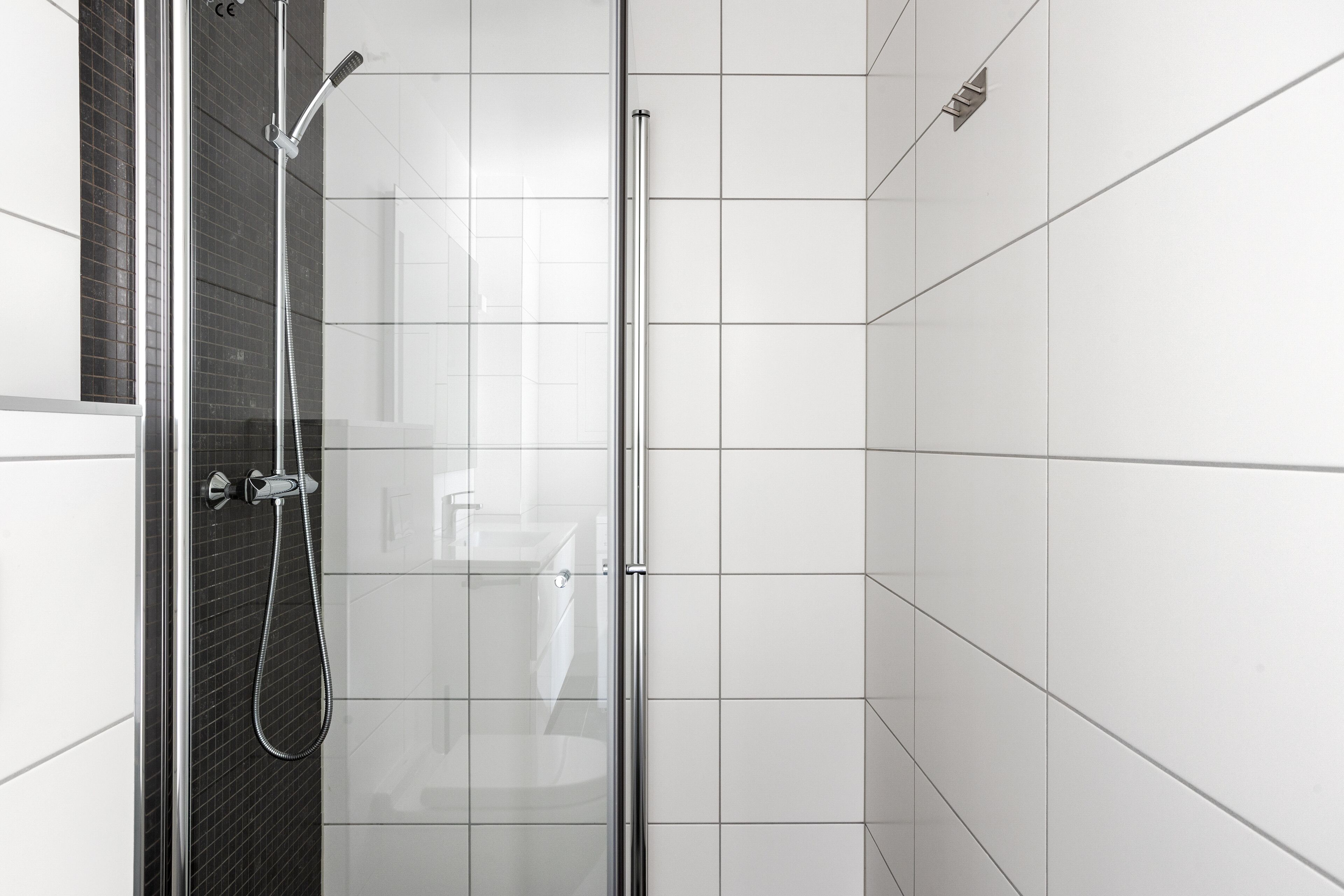 Un área de ducha moderna con puerta de vidrio, paredes de azulejos blancos y cabezal de ducha cromado.