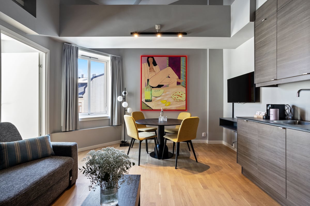 A modern living room with a sofa, dining table, chairs, and a vase of flowers.
