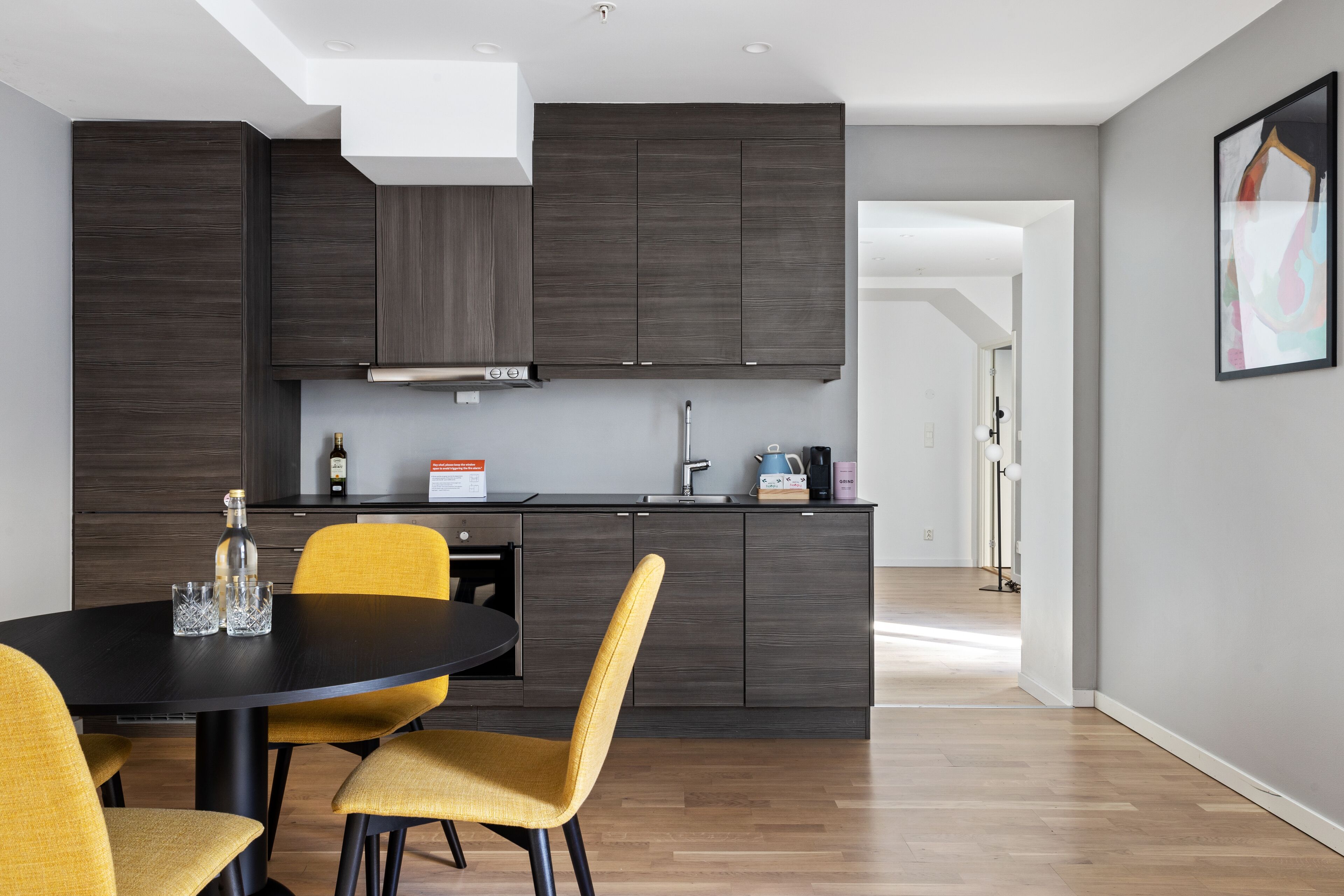 A modern kitchen with dark cabinetry, a black dining table, and yellow chairs.