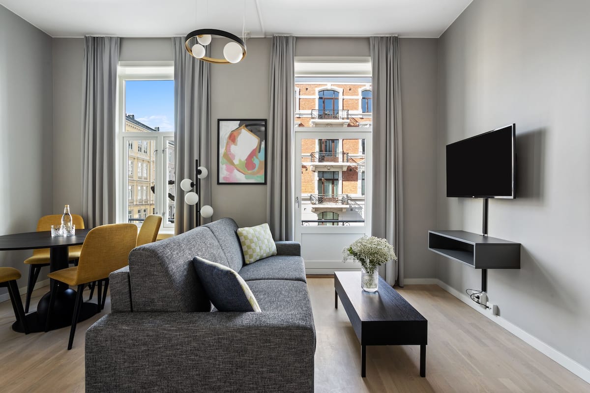 A modern living room with a grey sofa, yellow chairs, a dining table, and a TV on a stand.