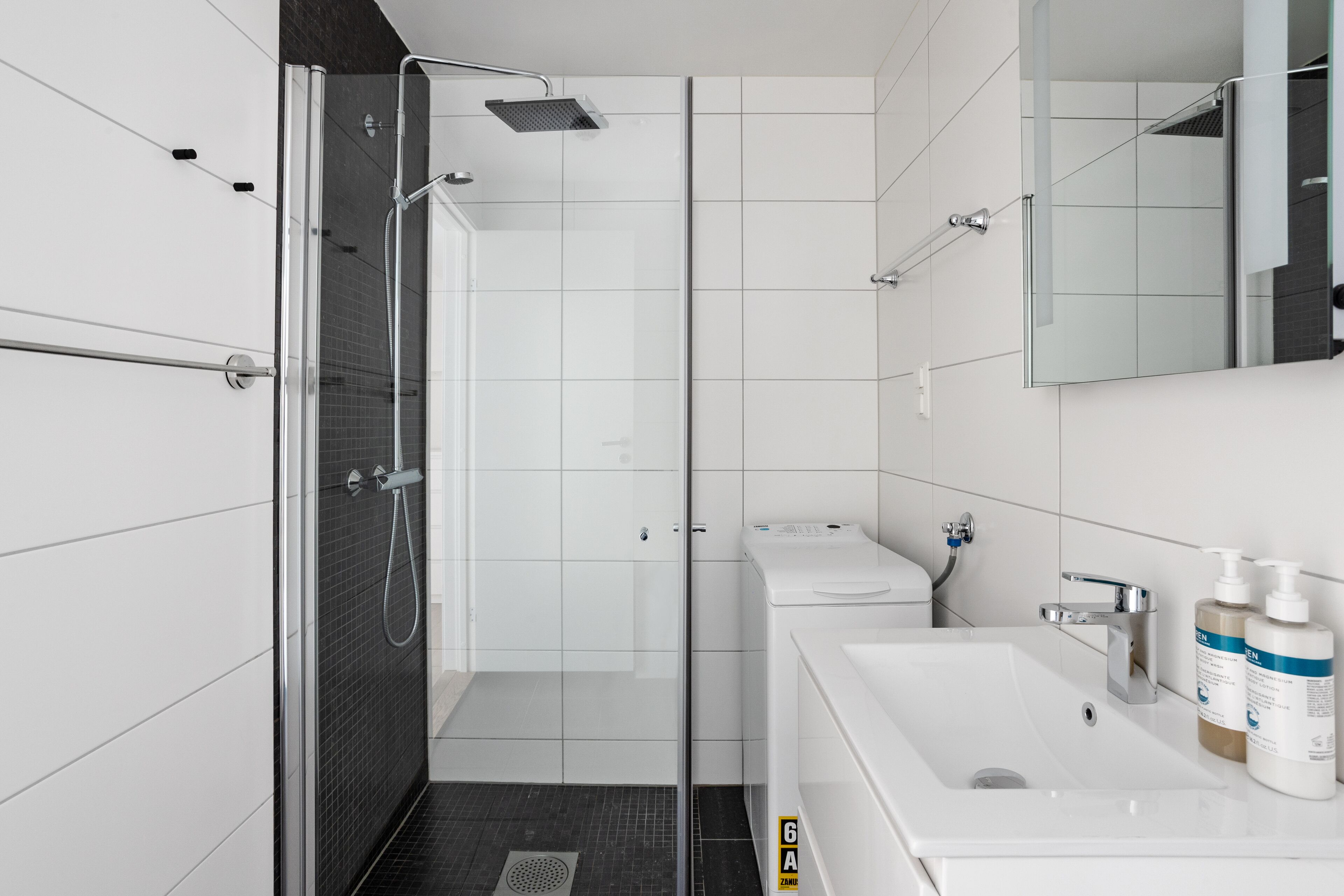 A modern bathroom with a glass-enclosed shower, a white sink, and a mirror.