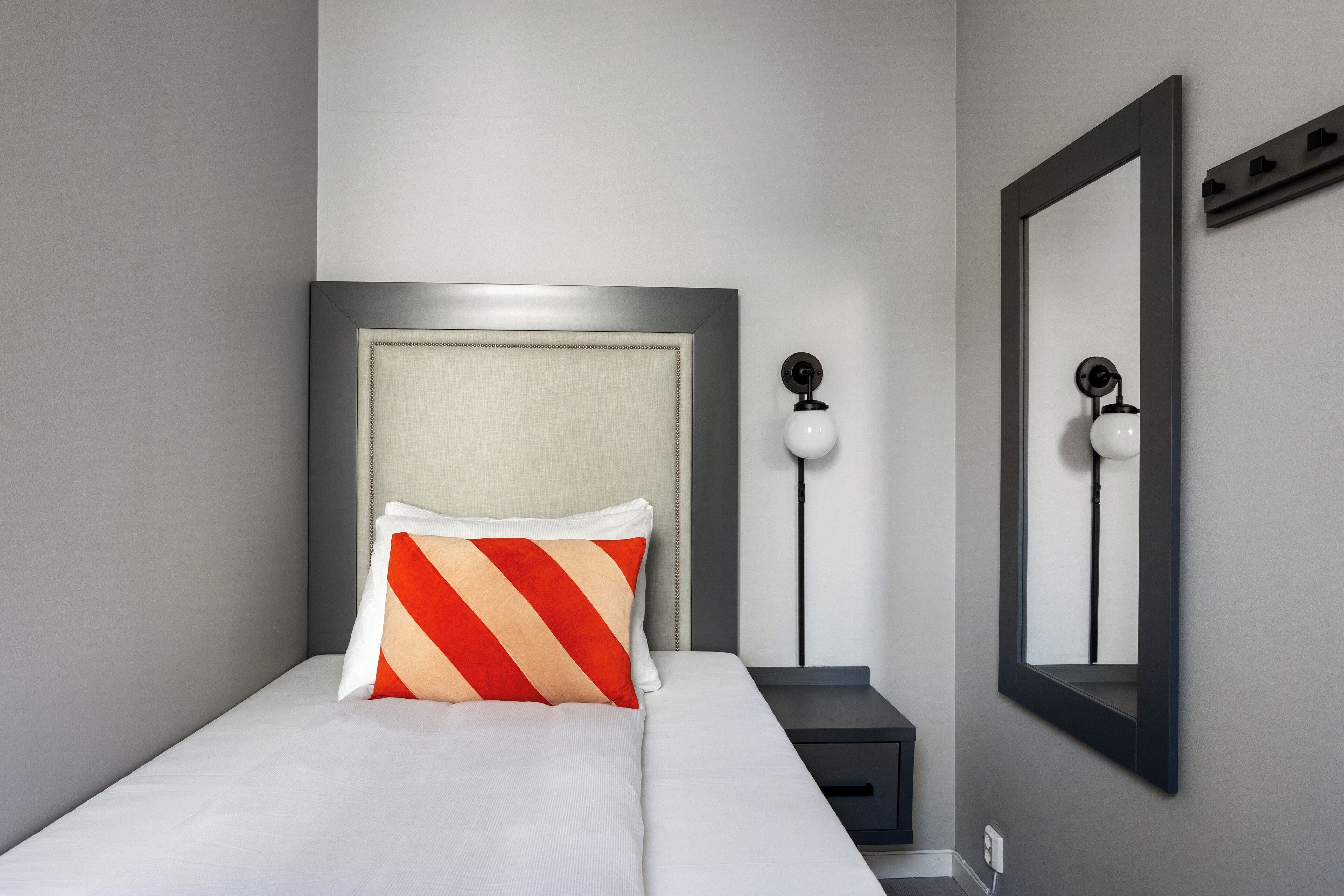 Un lit bien fait, avec un oreiller à rayures, une lampe de chevet et un miroir au mur.