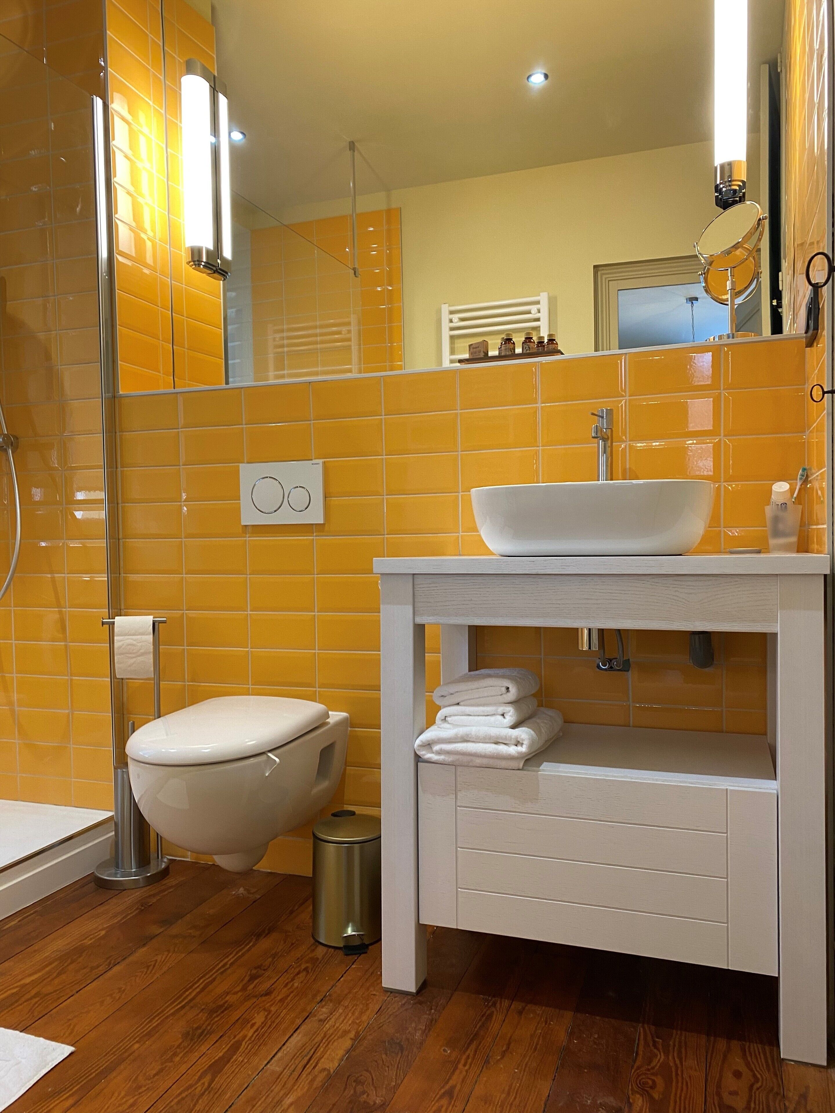 Un baño moderno con una pared de azulejos amarillos, un lavamanos blanco y un inodoro.