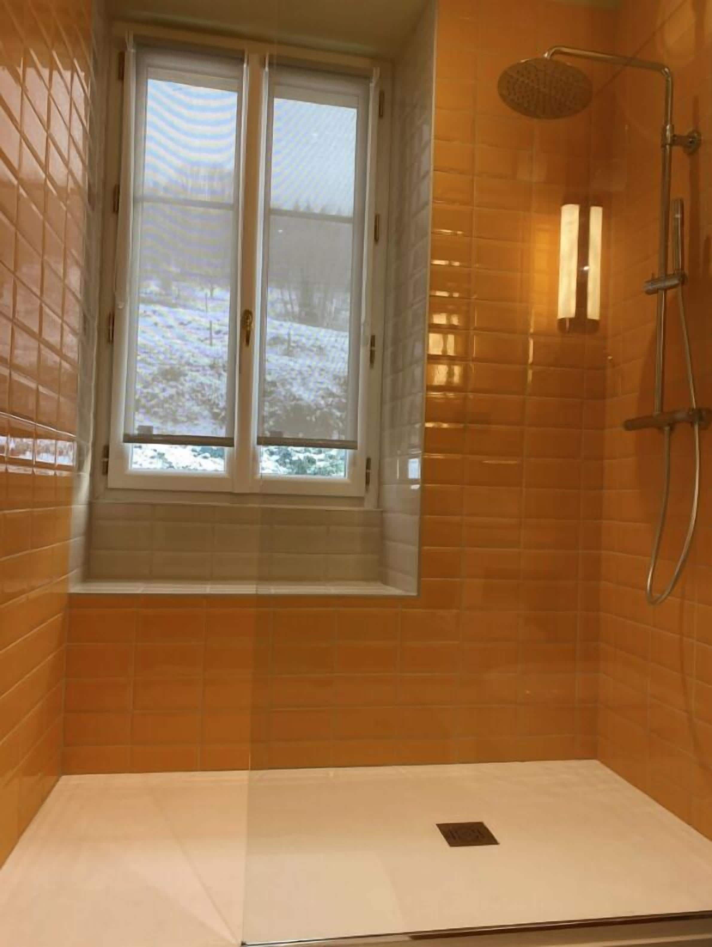 Douche met raam, oranje betegelde wanden en zichtbaar uitzicht.