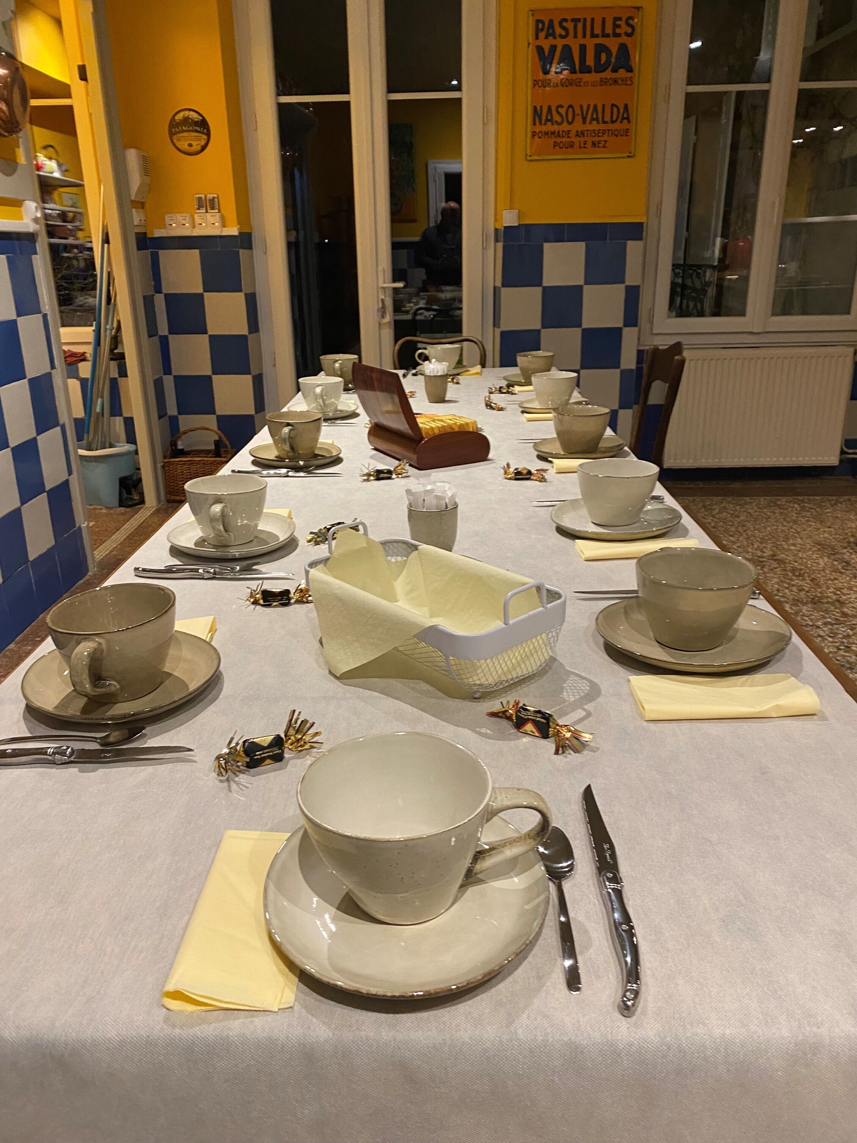 Une table à manger dressée avec des bols, des tasses et des couverts, et un panneau sur le mur faisant la publicité de pâtisseries.