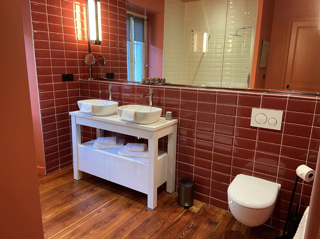 Une salle de bain avec deux lavabos, un miroir, des toilettes et une poubelle.