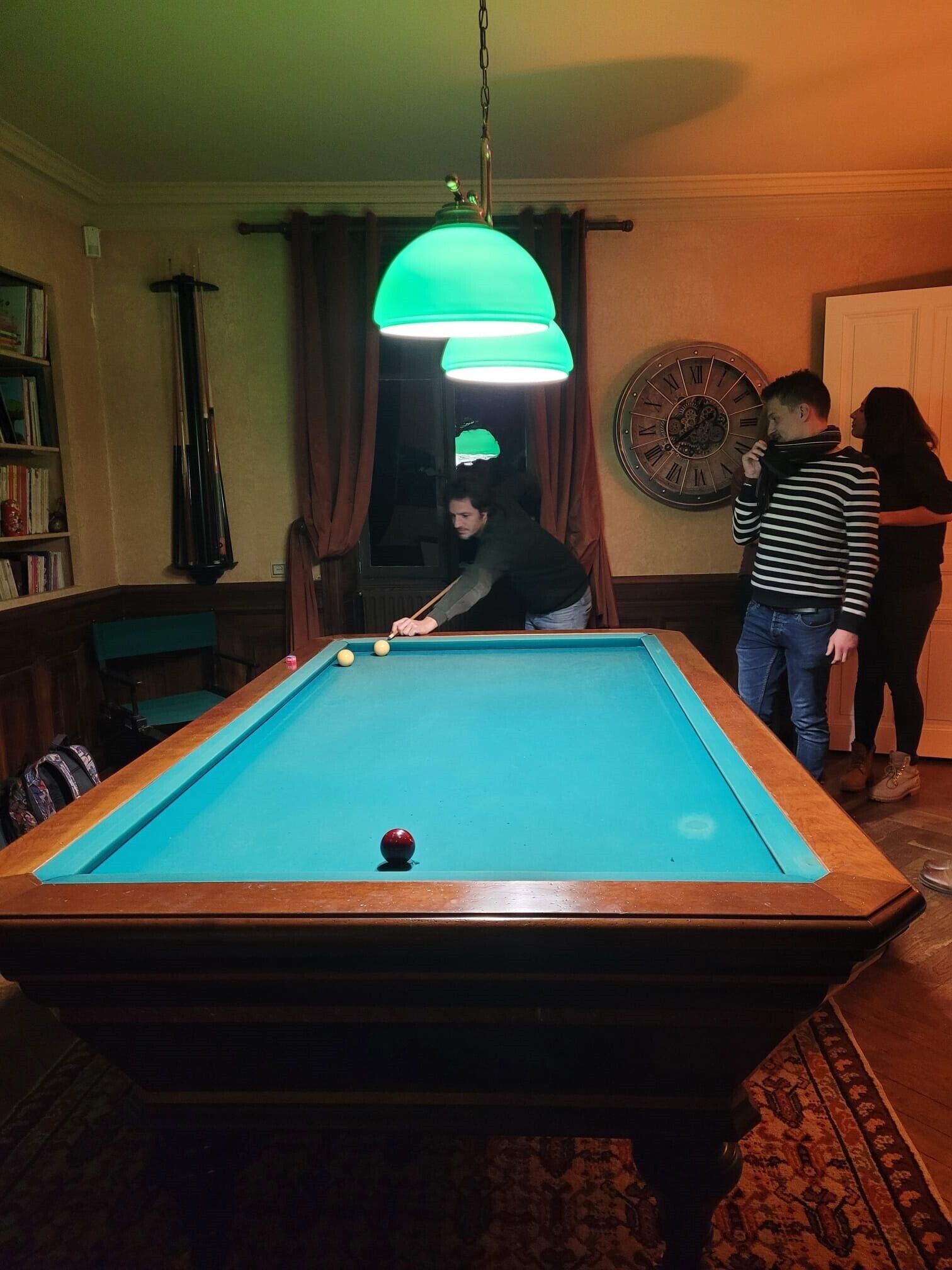 Una mesa de billar en una habitación con un reloj en la pared y una lámpara colgante.