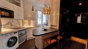 Een moderne keuken met witte kasten, een Bosch wasmachine, een bijzondere kroonluchter en een klein eethoekje met een stoel.