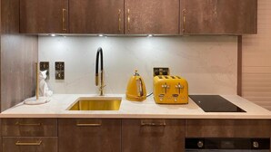 A kitchen with wooden cabinets, a stainless steel sink, a yellow kettle, and a yellow toaster. - Ailim House Serviced Cottage (St. Andrews)