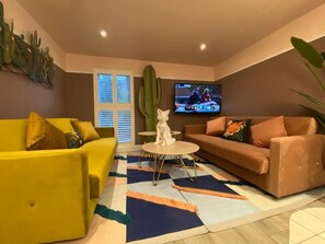 A living room with a yellow sofa, a brown sofa, a coffee table, a cactus, and a TV on the wall. - Ailim House Serviced Cottage (St. Andrews)