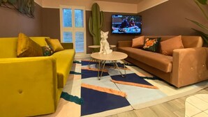 A living room with a yellow sofa, a brown sofa, a coffee table, and a TV mounted on the wall. - Ailim House Serviced Cottage (St. Andrews)