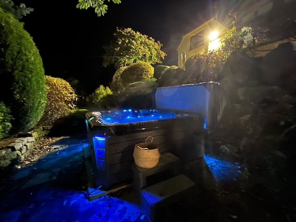 An outdoor hot tub with a stone surround, a basket, and a house in the background. - Ailim House Serviced Cottage (St. Andrews)