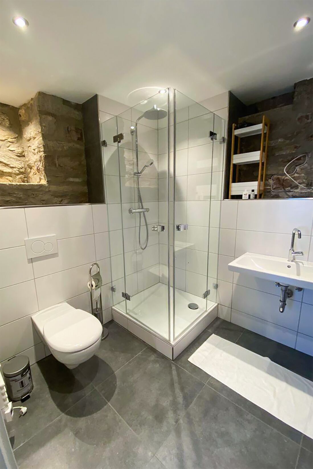 A modern bathroom with a glass-enclosed shower, a white toilet, and a sink with a mirror.