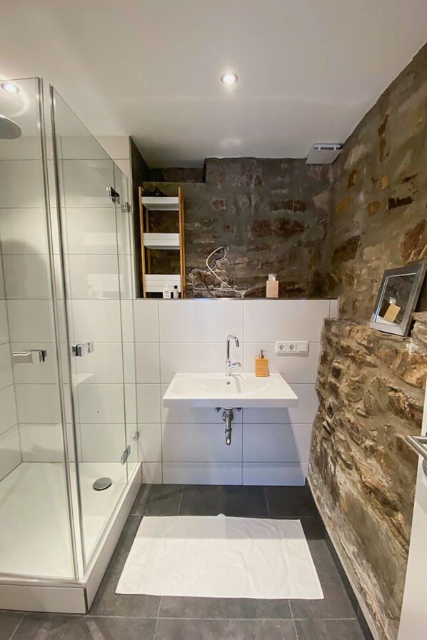A bathroom with a glass shower enclosure, a white sink, and a stone accent wall. - Hallgarter Zange (Oestrich-Winkel)
