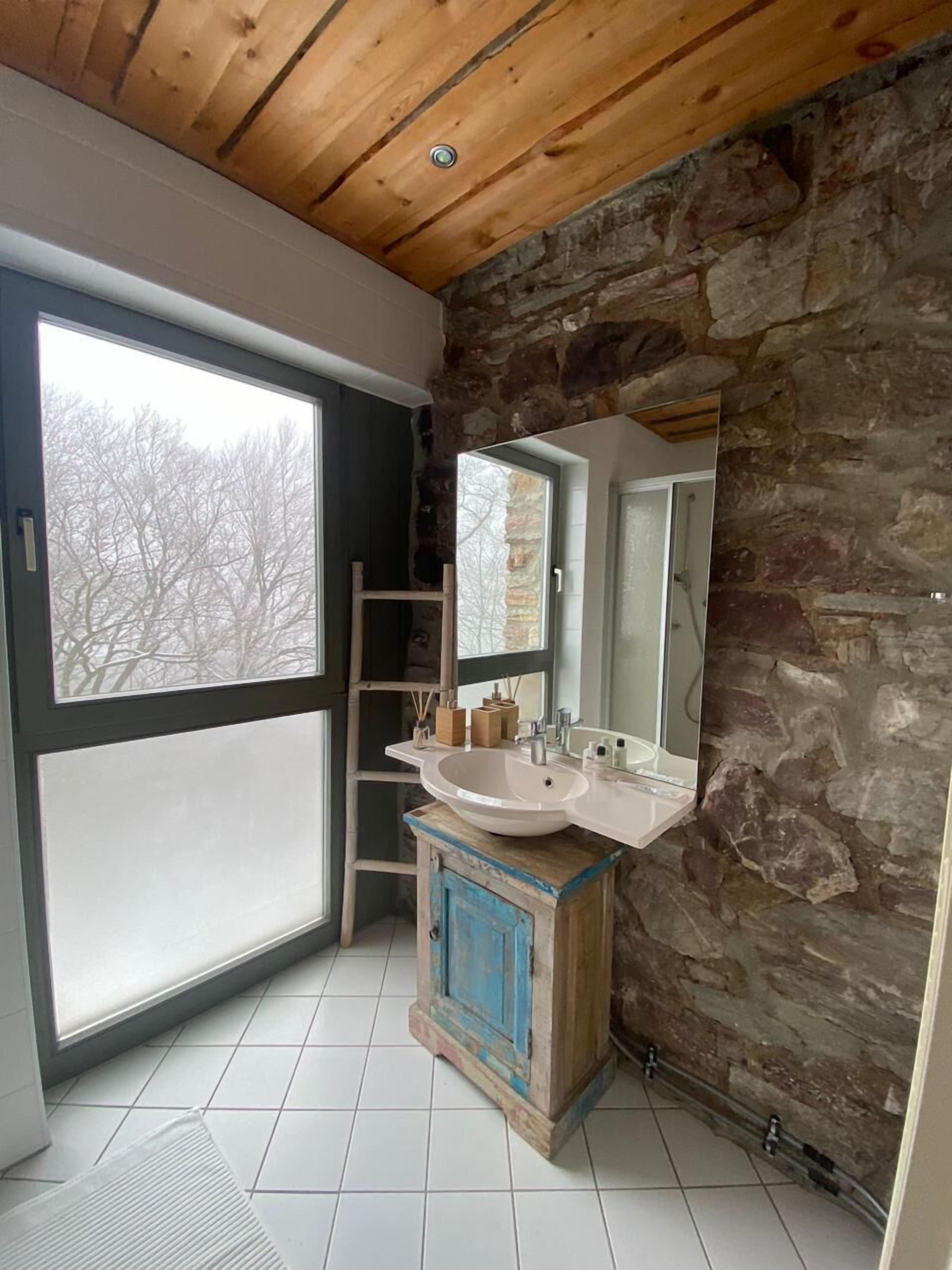 A bathroom with a stone wall, a large window, and a wooden ceiling.