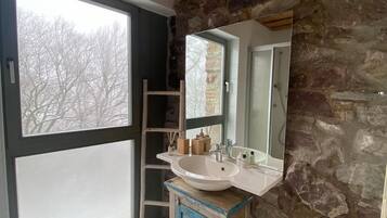 A bathroom with a stone wall, a large window, and a wooden ceiling.