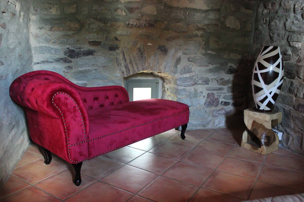 A red velvet sofa in a stone-walled room with a tiled floor.