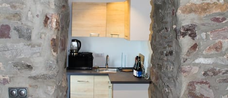 A narrow stone archway leading into a modern kitchen with wooden cabinets and a coffee machine.